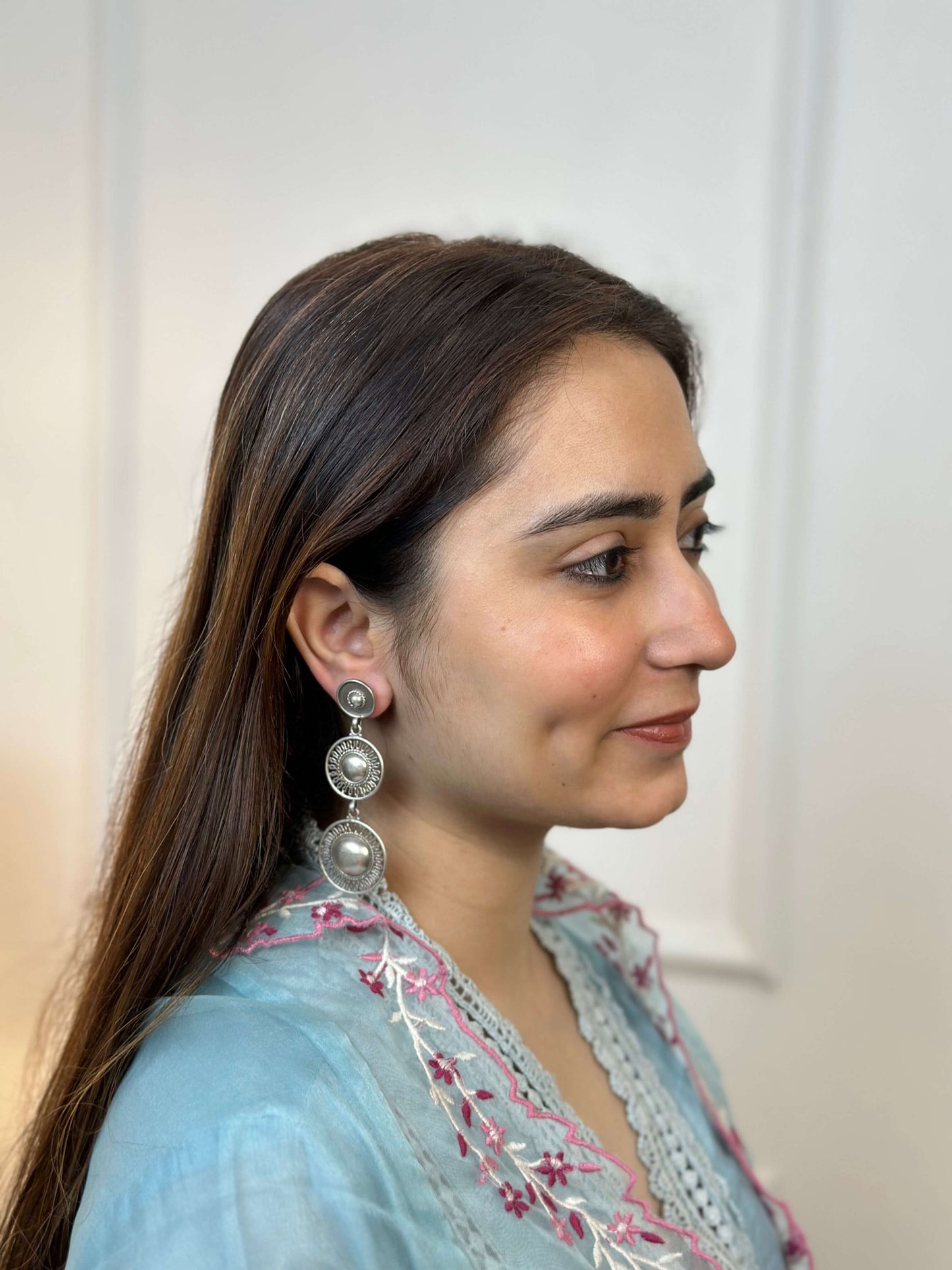 Woman wearing a light blue embroidered top with a plain background