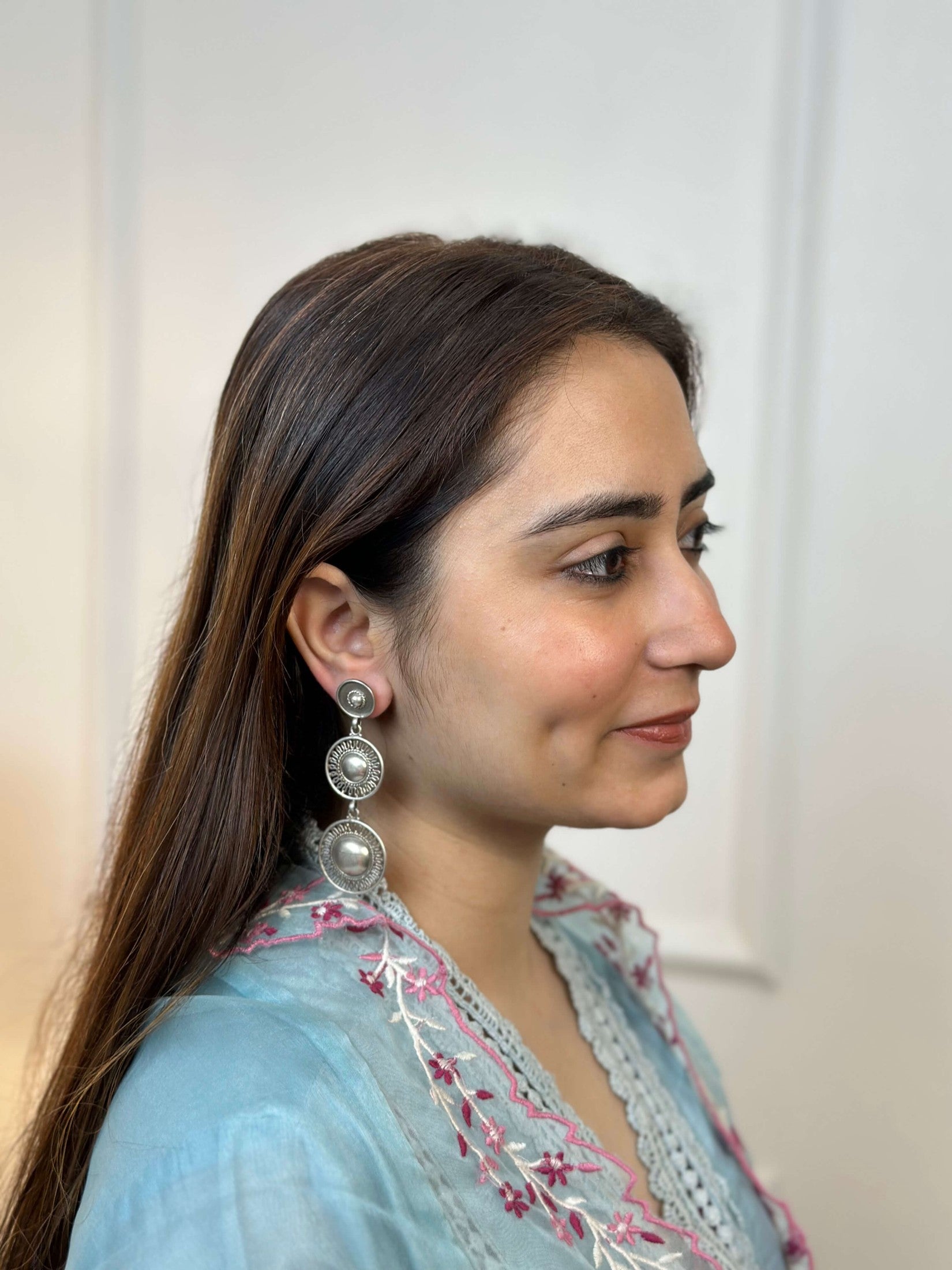 Woman wearing a light blue embroidered top with a plain background