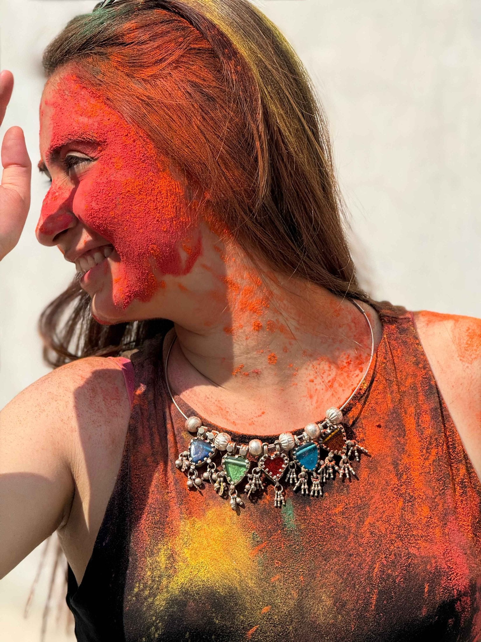 Person with colorful face paint and silver jewelry, possibly celebrating Holi festival.