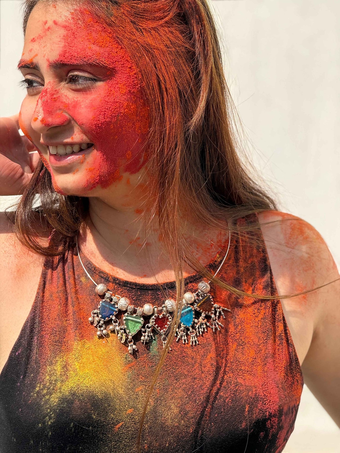 Woman with colorful face paint and body art, wearing a necklace with colorful stones.