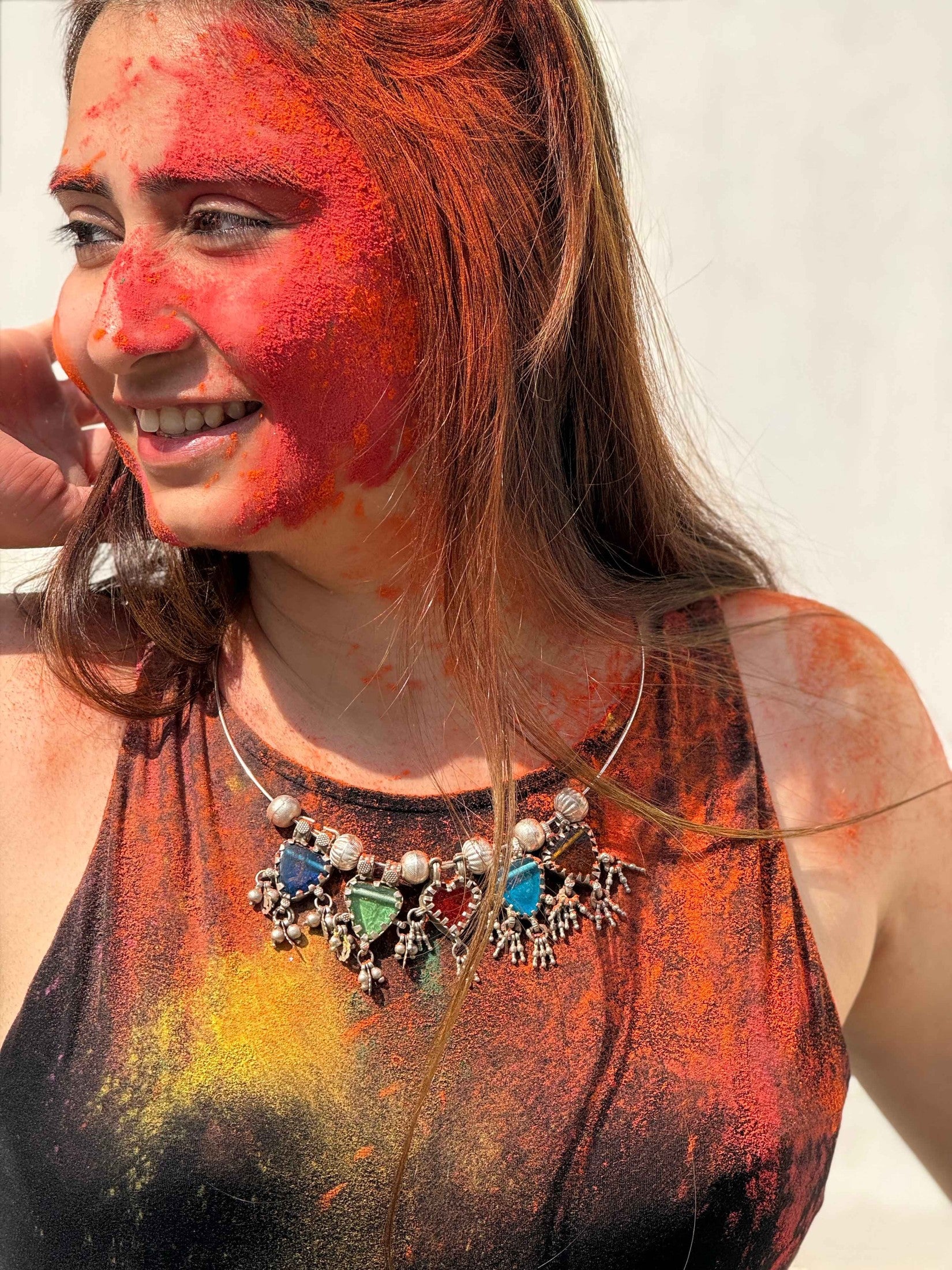 Woman with colorful face paint and body art, wearing a necklace with colorful stones.