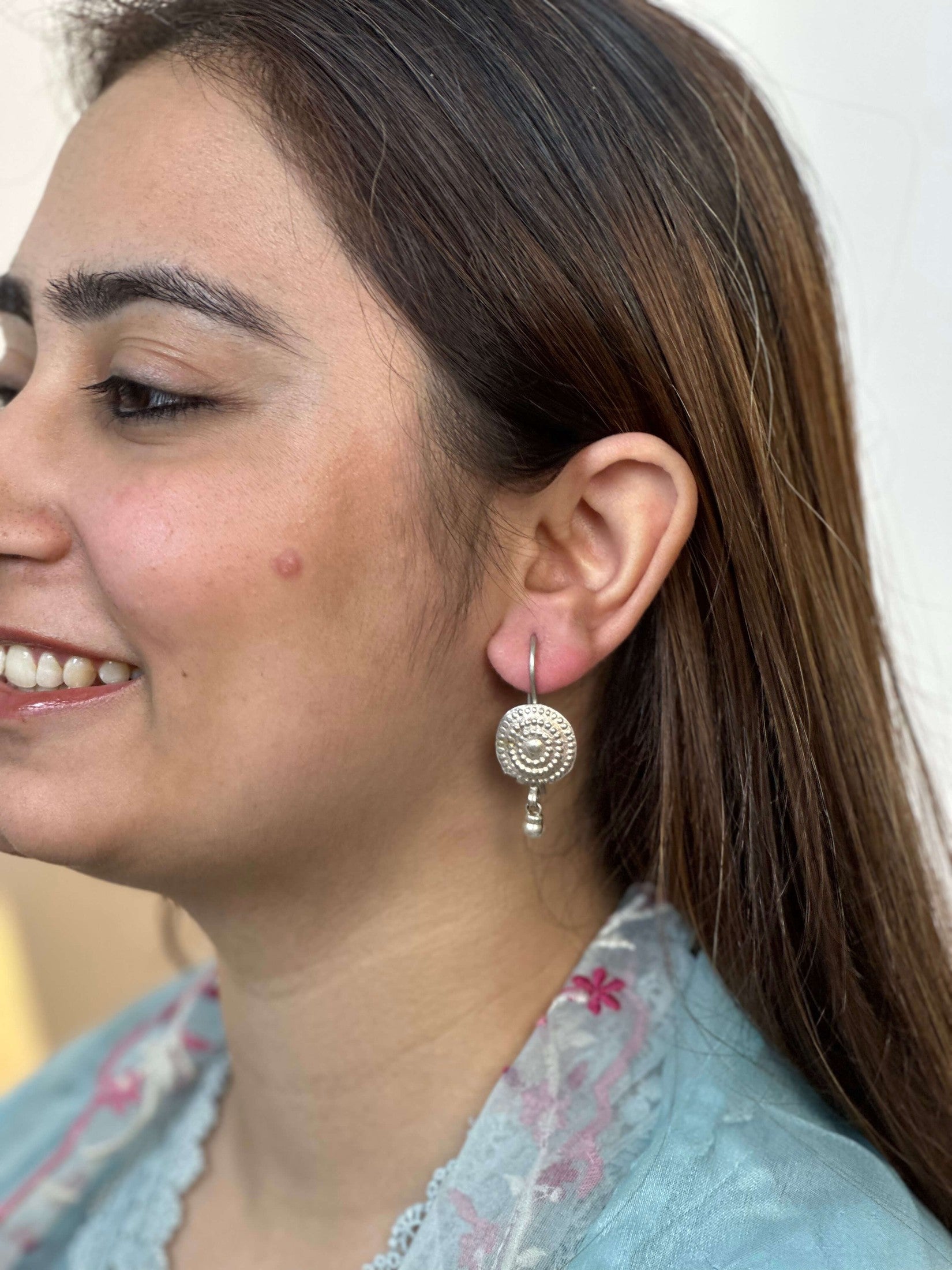 Close-up of a woman wearing silver earrings with a plain background