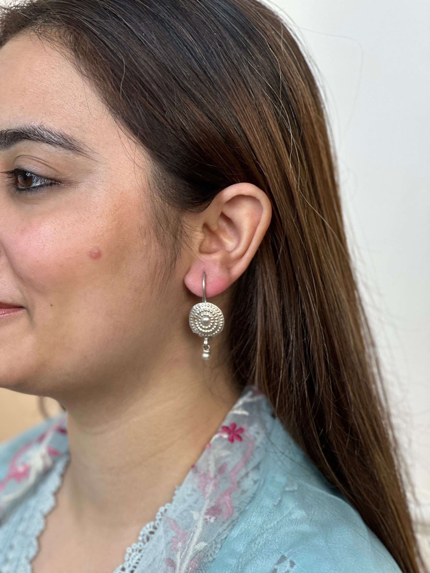 Close-up of a woman wearing silver earrings with a plain background