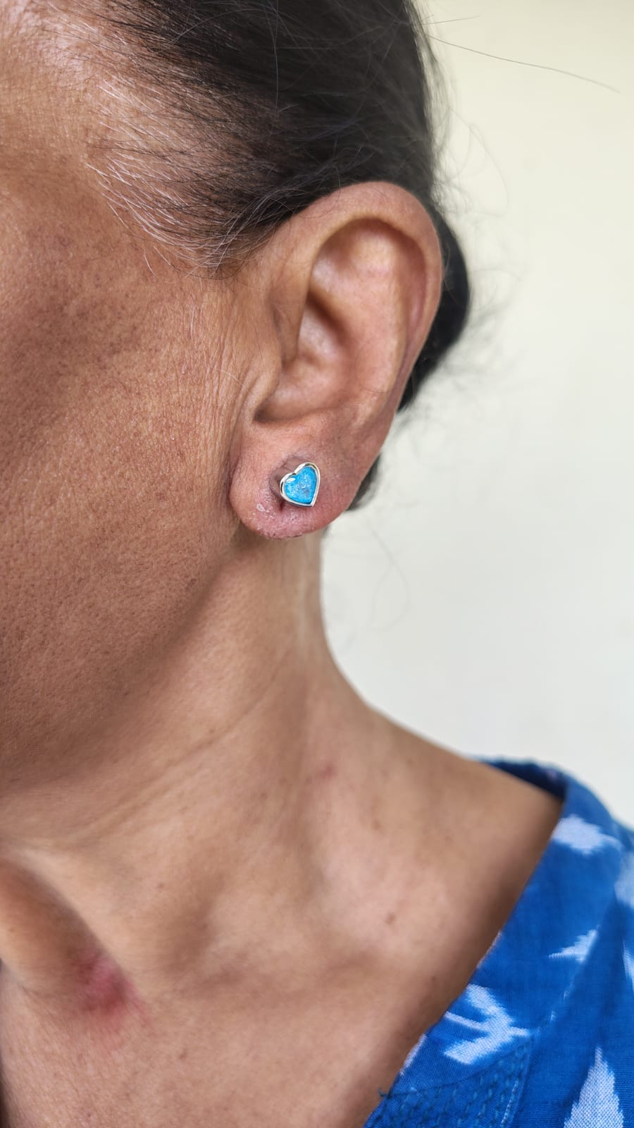 Close-up of an ear wearing a blue heart-shaped earring with a blurred background