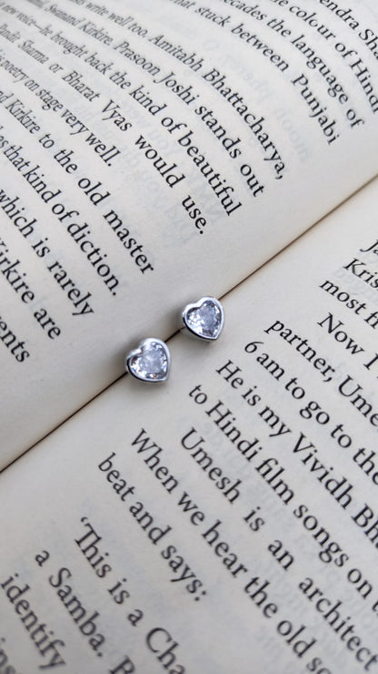 Heart-shaped and round stud earrings on a book page with text.