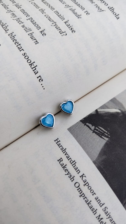 Heart-shaped blue 92.5 silver earrings on an open book with text.