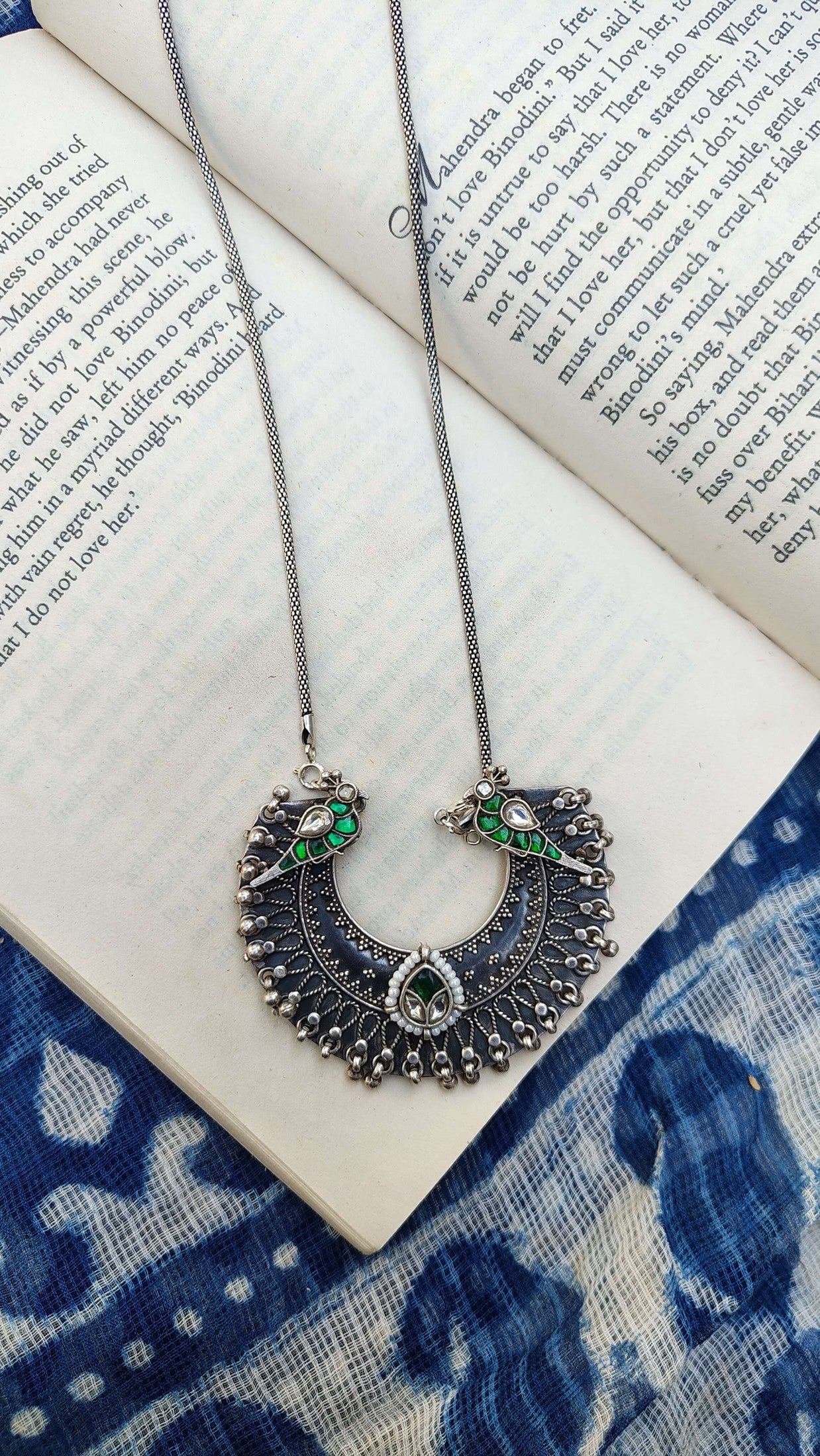 Decorative necklace with green and white birds on an open book with blue floral patterns.