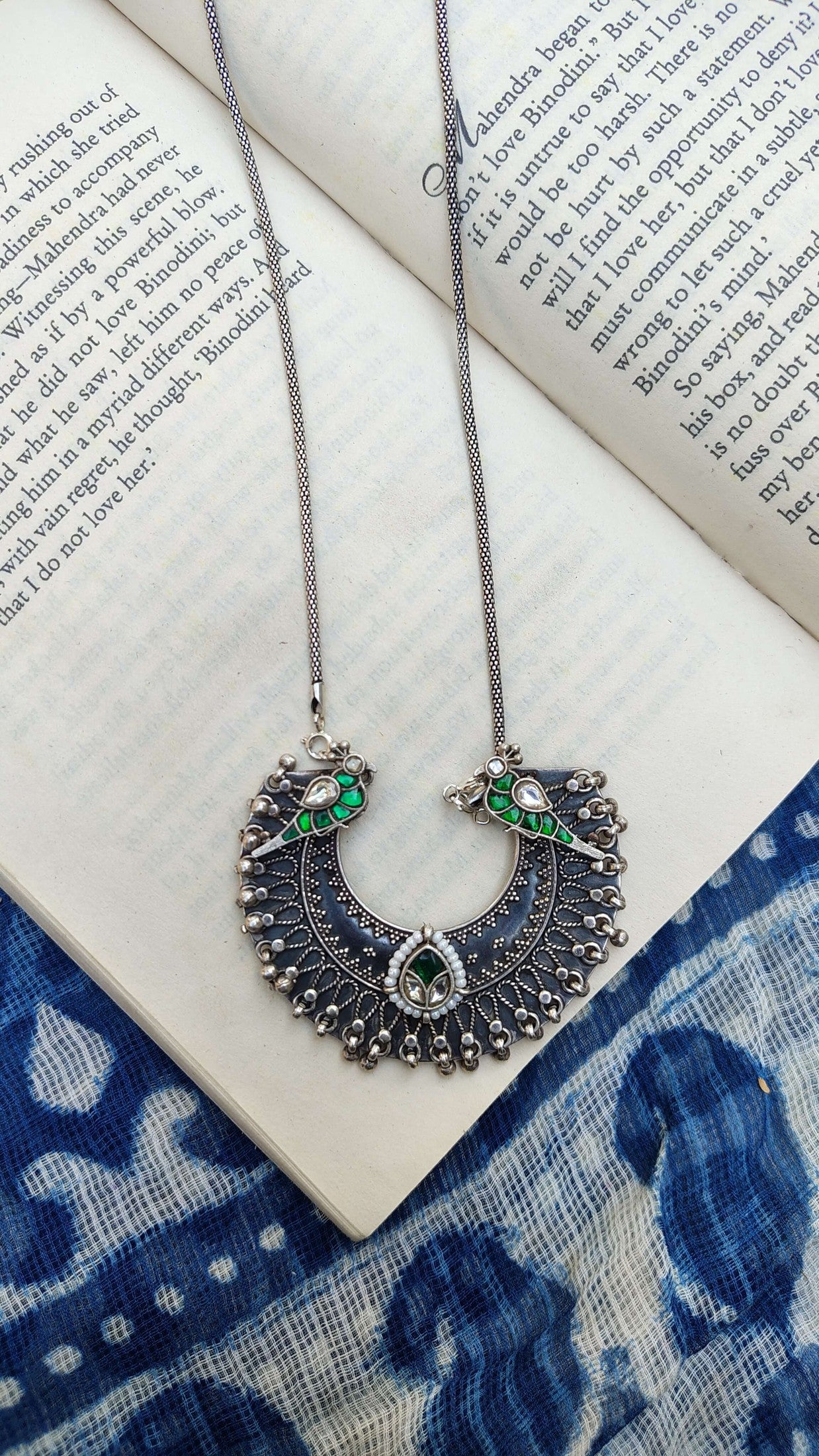 Decorative necklace with green and white kundan stones on an open book