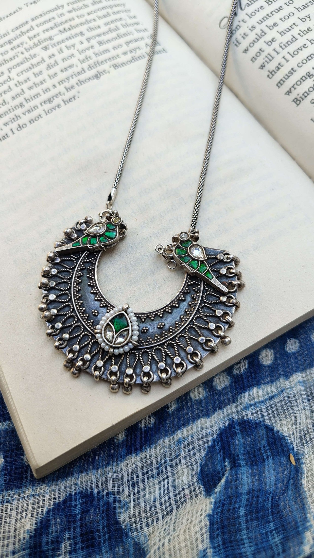Ornate silver necklace with green gemstones on an open book