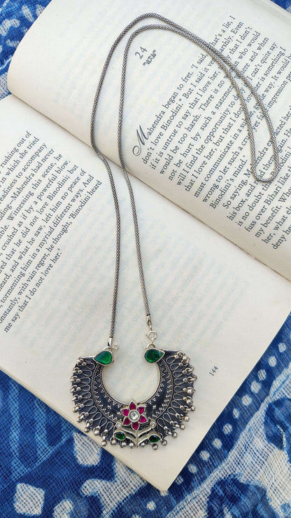 Decorative necklace with green and red stones on an open book