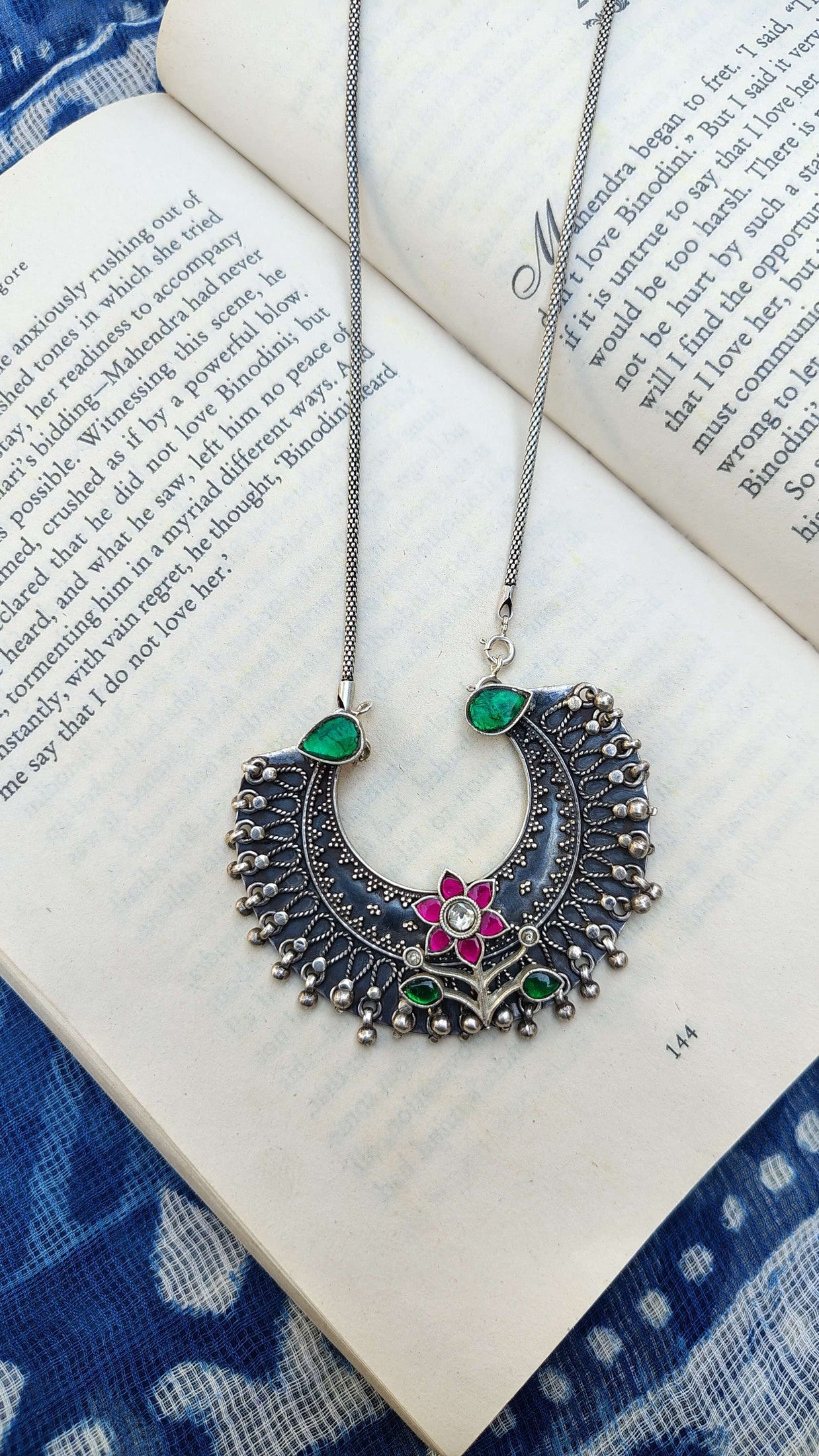 Ornate necklace with green and red accents on an open book