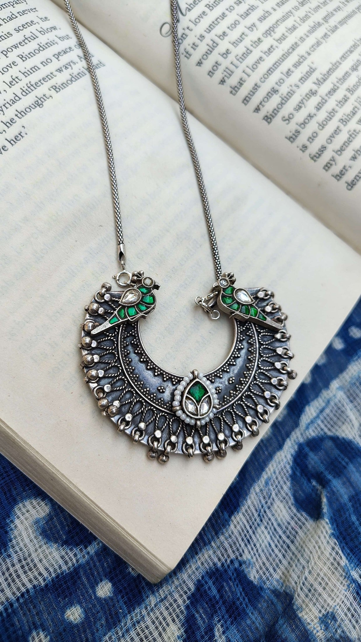 Ornate silver necklace with green kundan stones on an open book