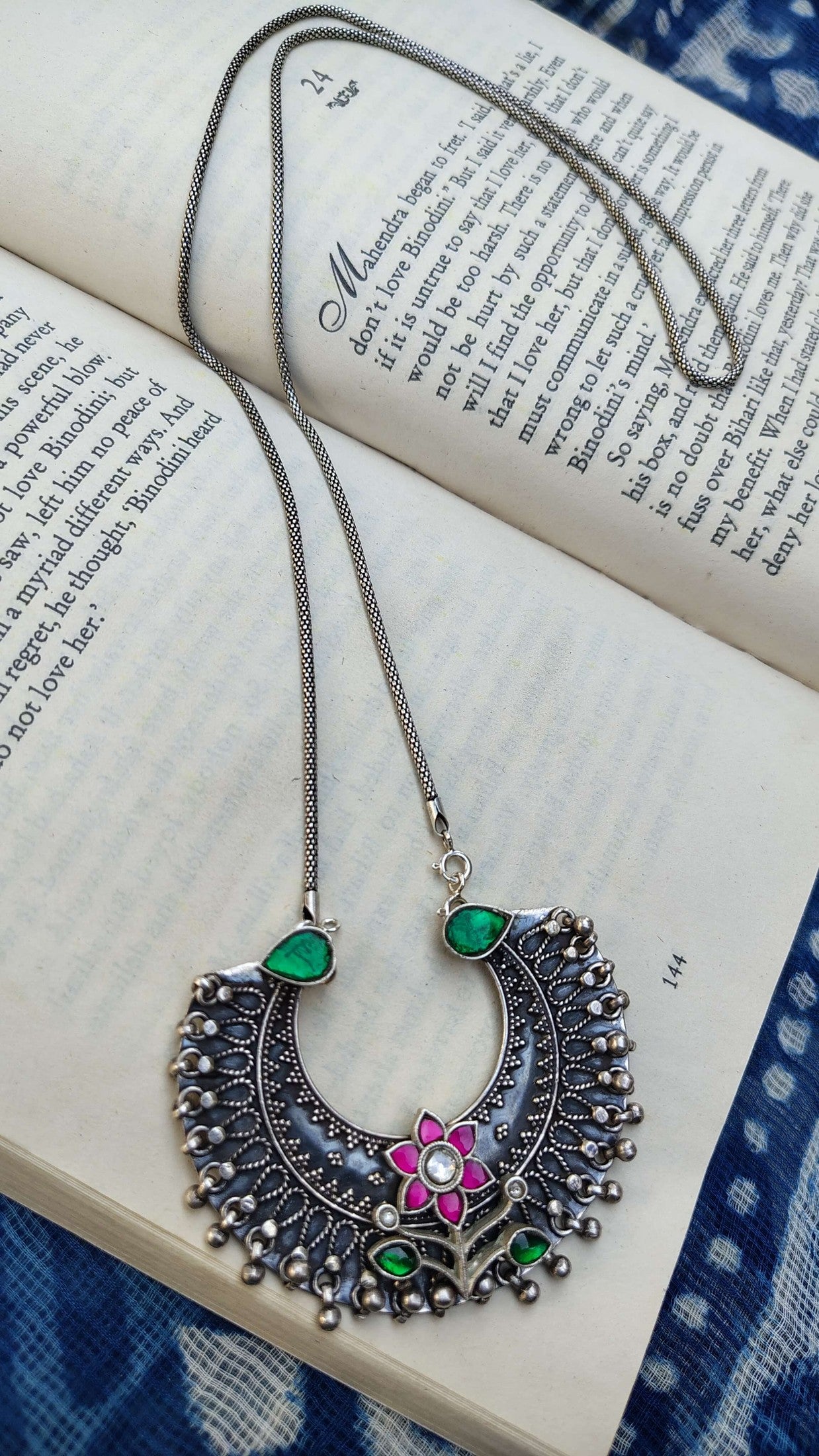 Decorative necklace with green and pink kundan on an open book