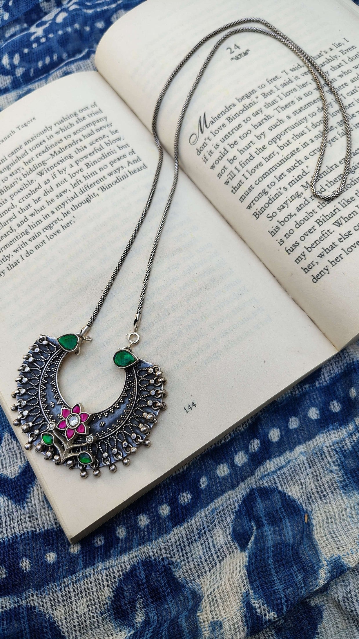 Ornate necklace on an open book with a blue patterned fabric background