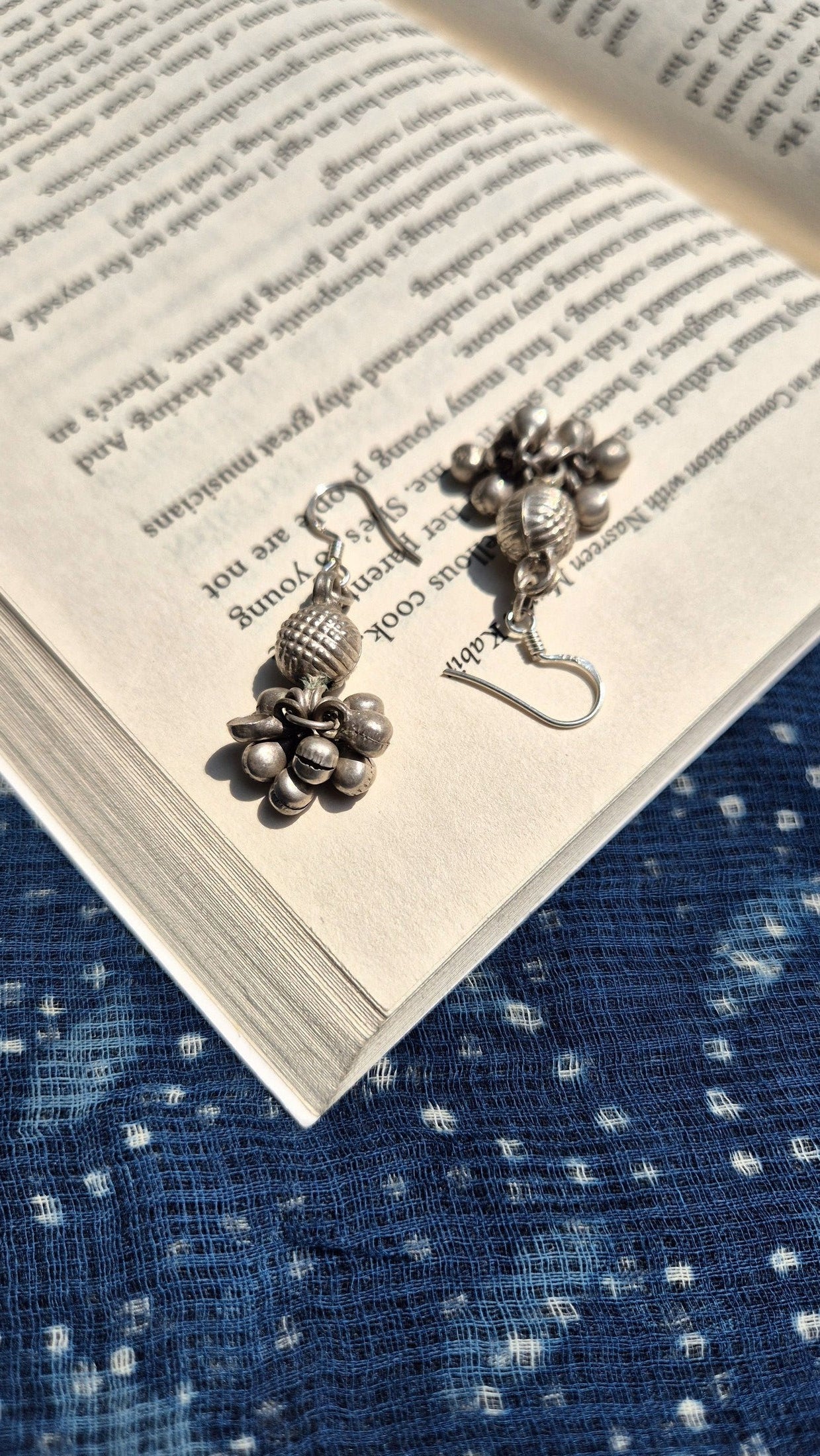Pair of silver earrings on an open book with a blue textured fabric background