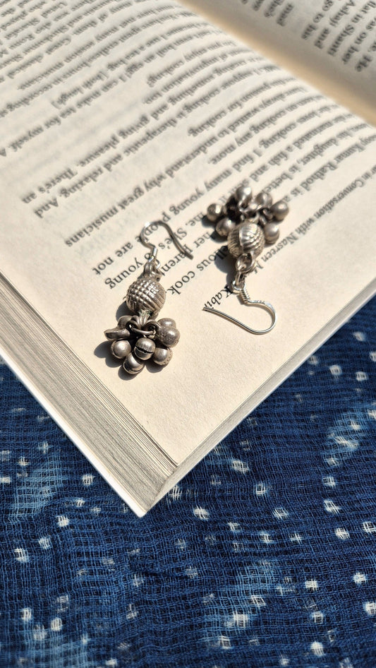 Pair of silver earrings on an open book with a blue textured fabric background