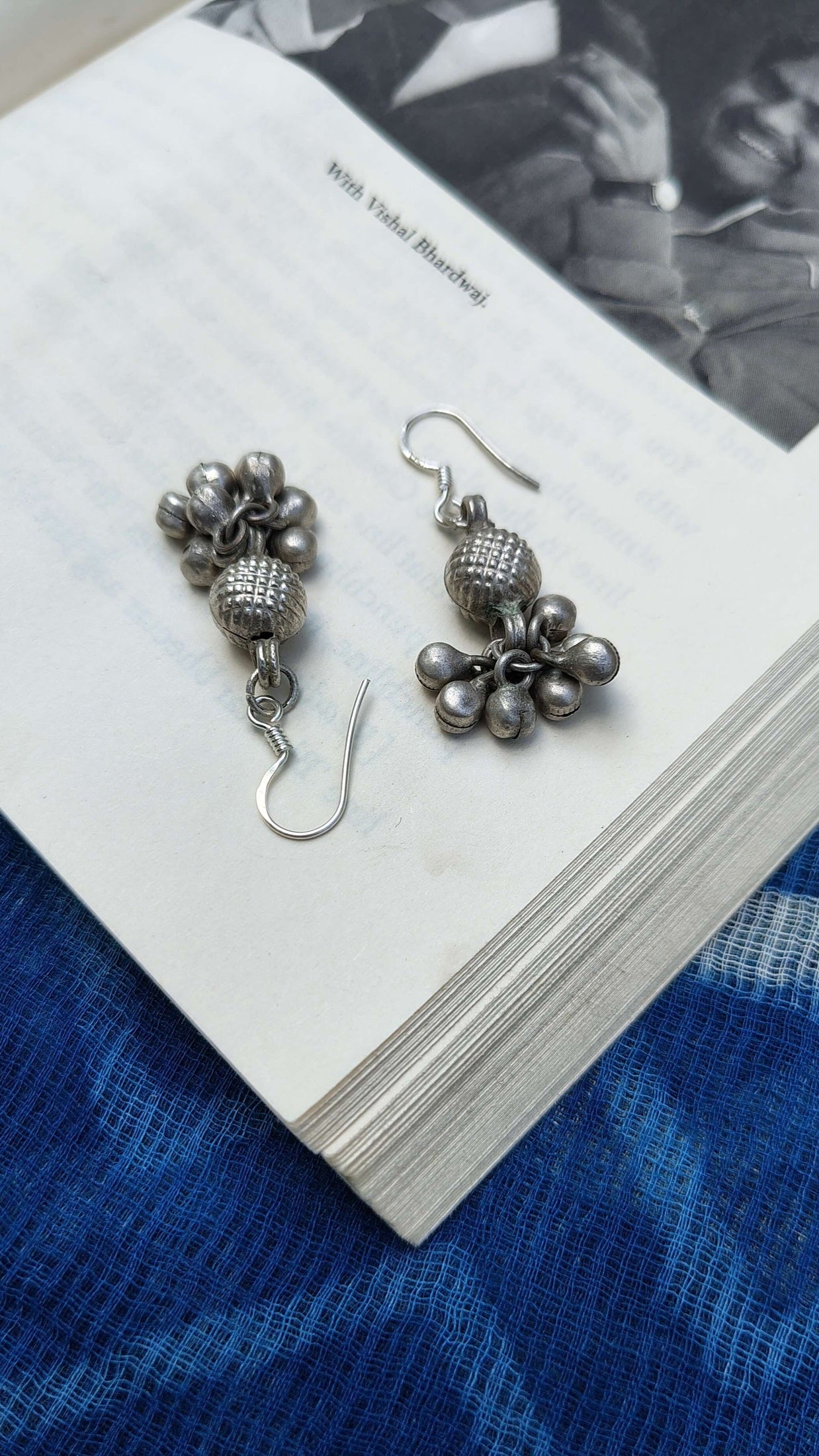 Silver earrings on a book with a blue fabric background