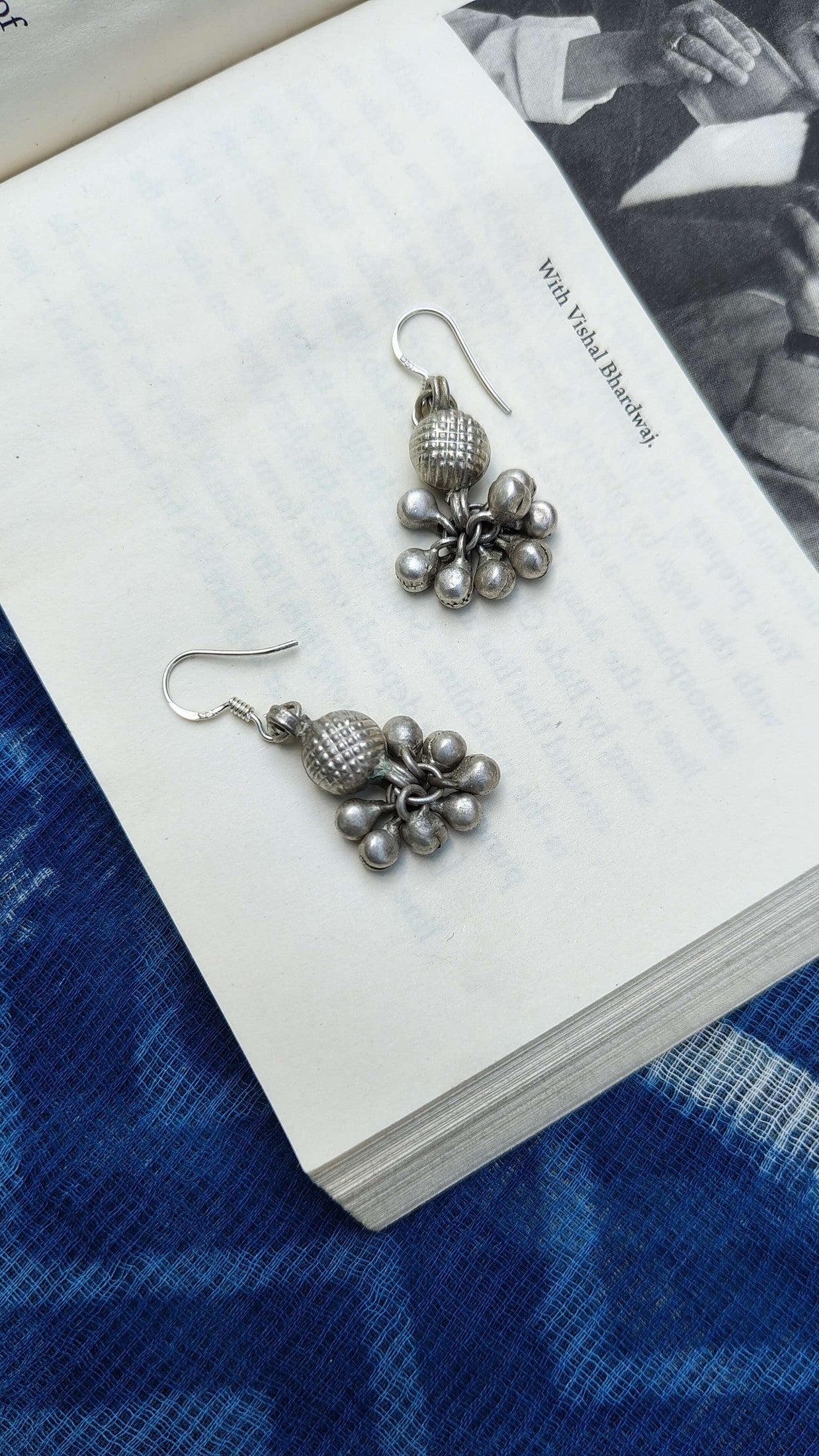 Pair of silver floral earrings on a white card with a blue fabric background