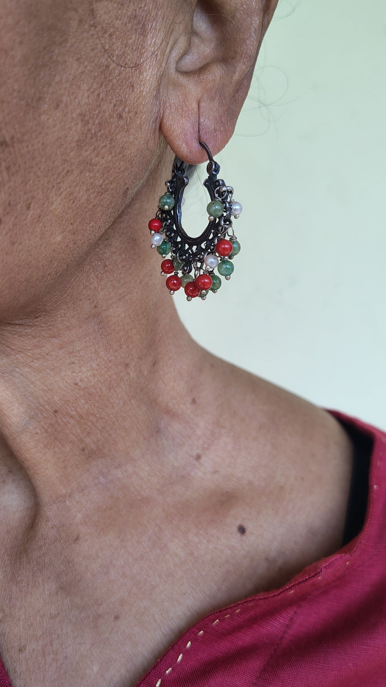 Close-up of a person's ear with pure silver hoops with gemstones on a plain background