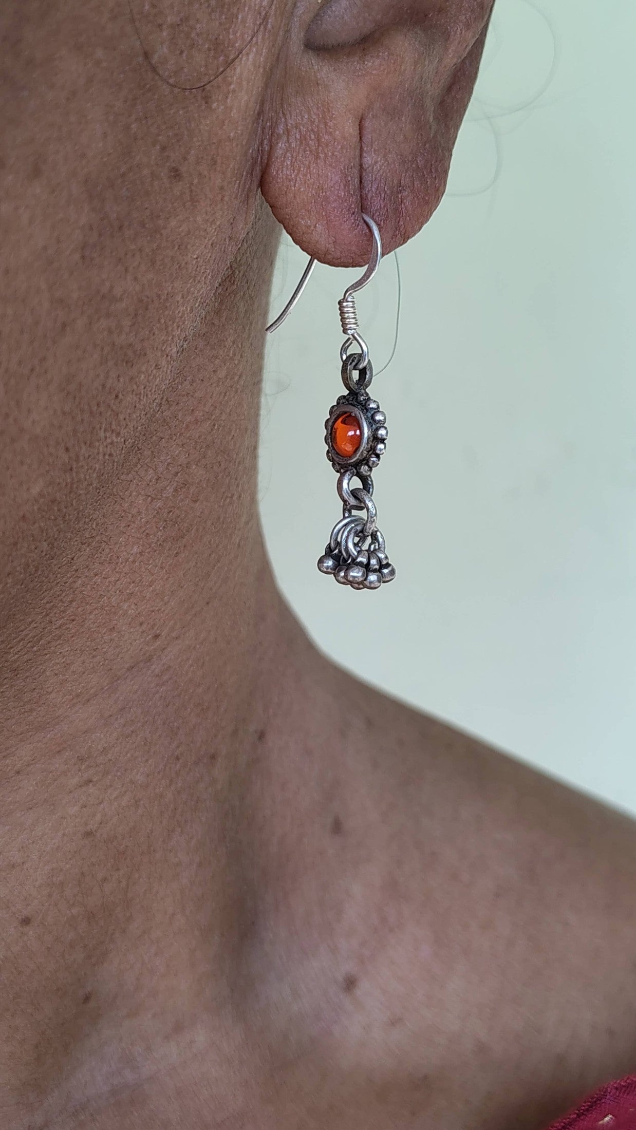 Close-up of a person wearing silver earrings with a red gemstone on a neutral background