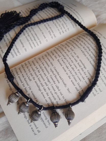 A cord necklace with five metallic silver conical beads and a tassel, arranged on the pages of an open book.