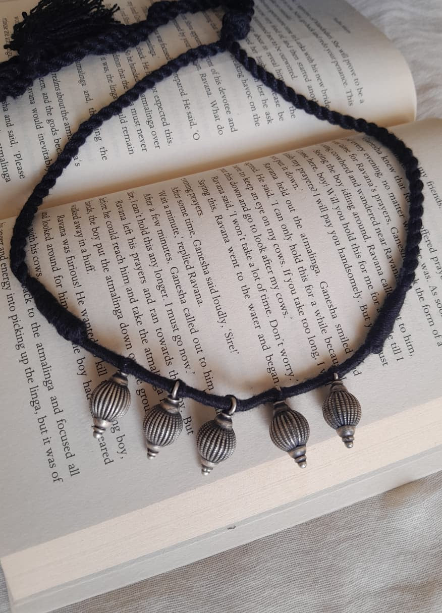 A black braided cord necklace with four silver-toned metal pendant beads, arranged on the pages of an open book.