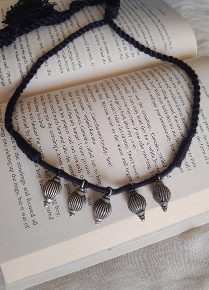 A black braided cord necklace with four silver-toned metal pendant beads, arranged on the pages of an open book.