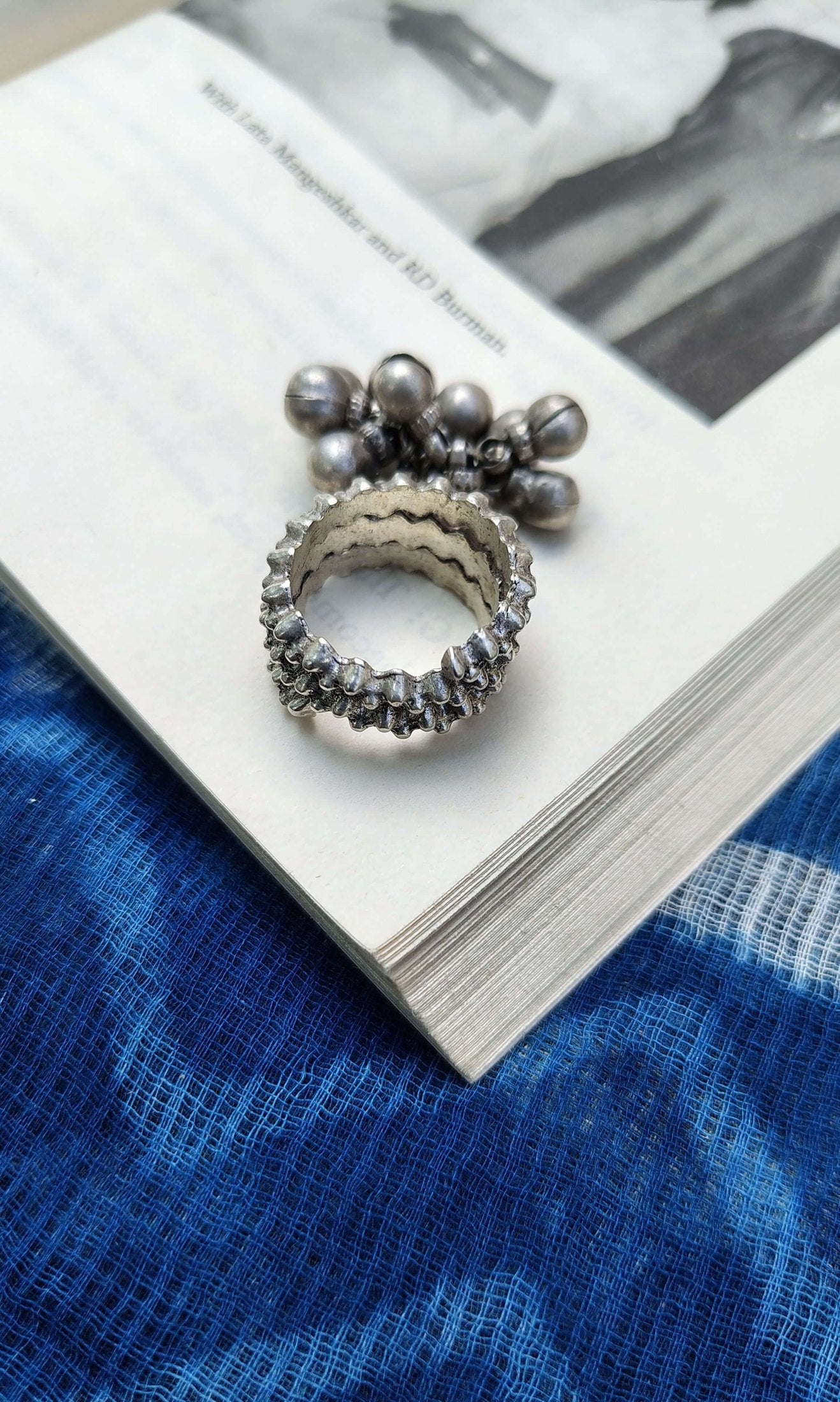 Silver ring with floral design on a book with a blue fabric background