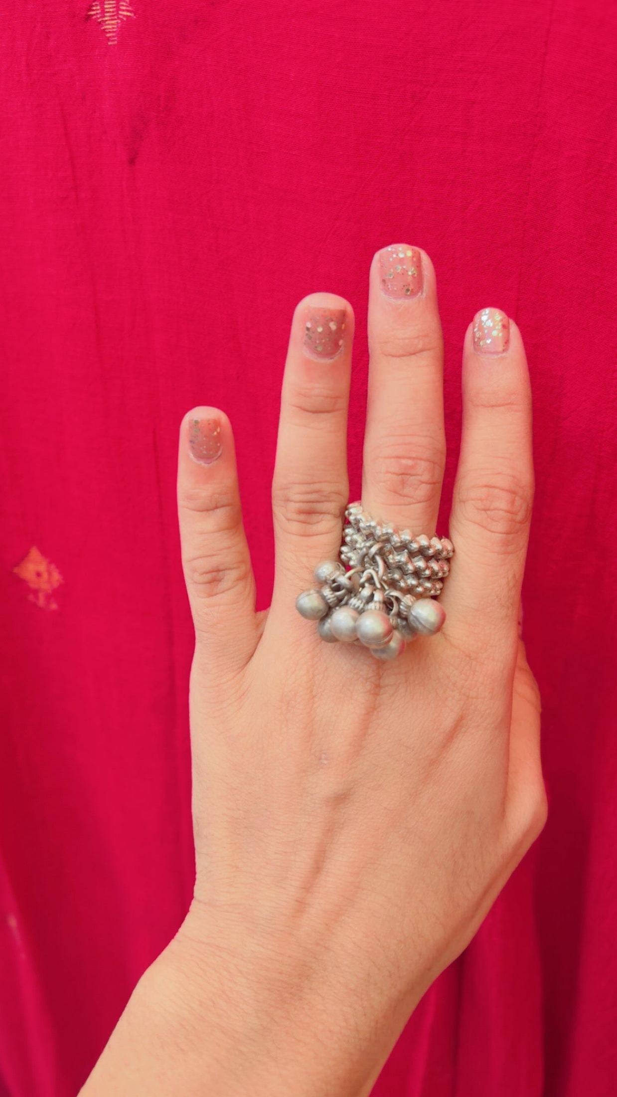 Hand wearing a silver ring with ghungroos against a red background