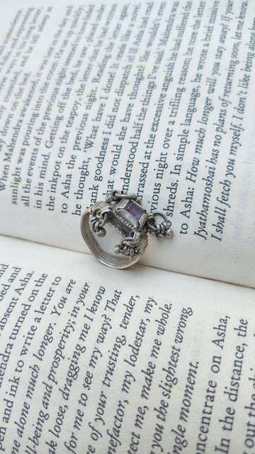 Silver ring with a purple gemstone on an open book