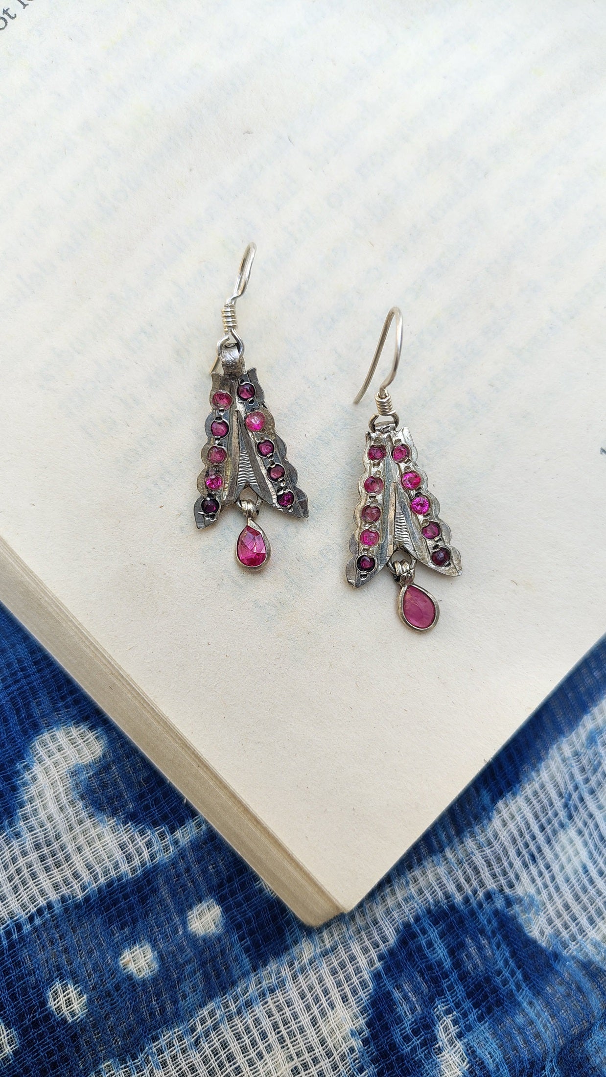 Pair of silver earrings with pink gemstones on a white surface with a blue patterned fabric background