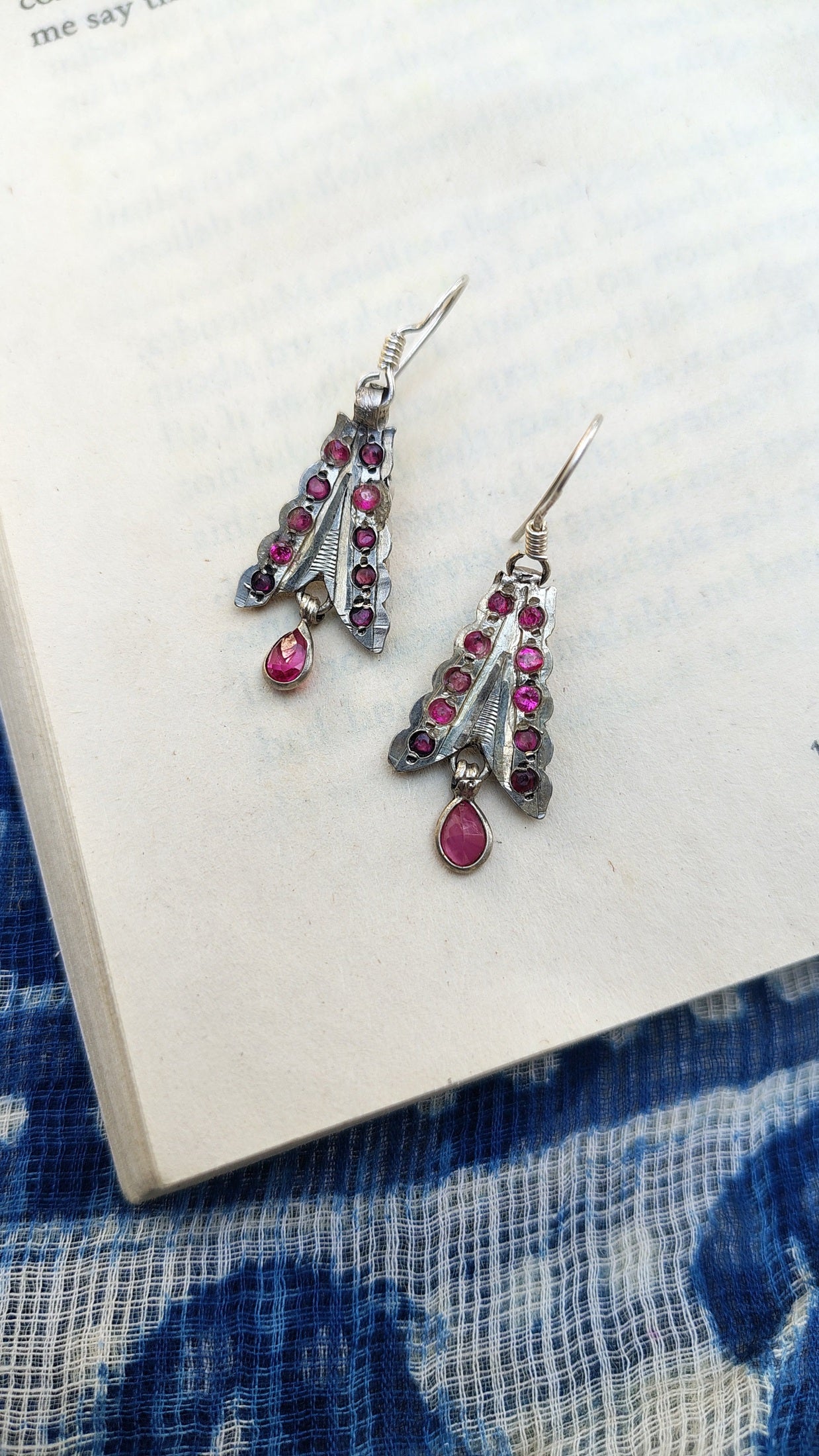 Silver earrings with pink gemstones on a white surface with blue fabric background