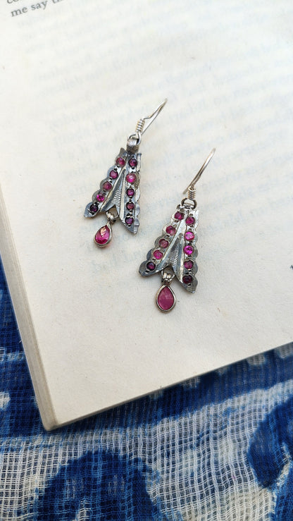 Silver earrings with pink gemstones on a white surface with blue fabric background