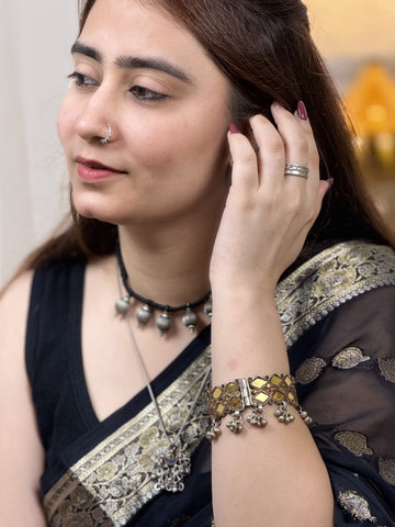 A woman wearing a black and gold sari with silver jewelry, including a silver ring on her finger and a silver bracelet on her wrist, posing indoors.