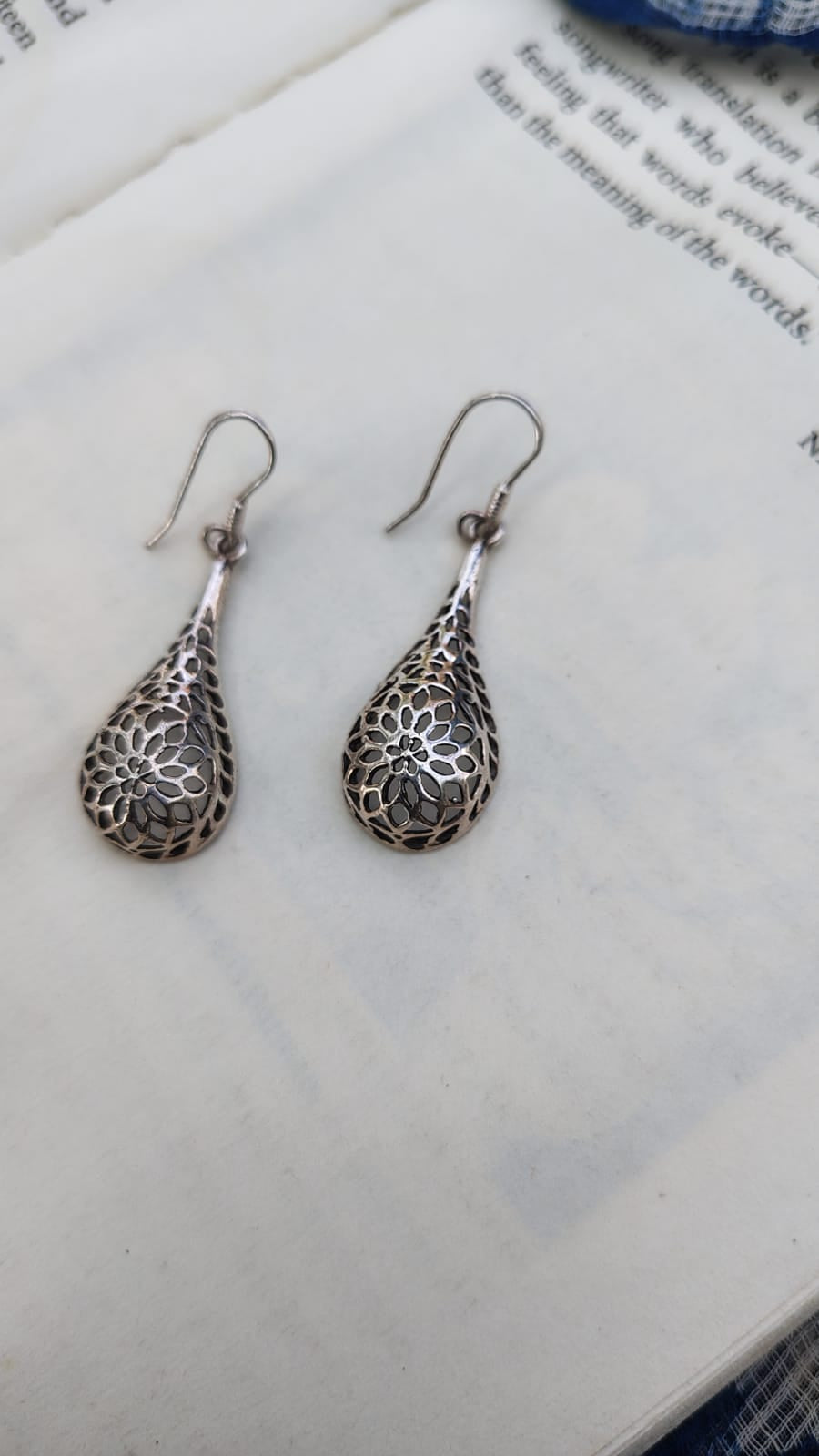 Pair of silver teardrop earrings on a textured surface
