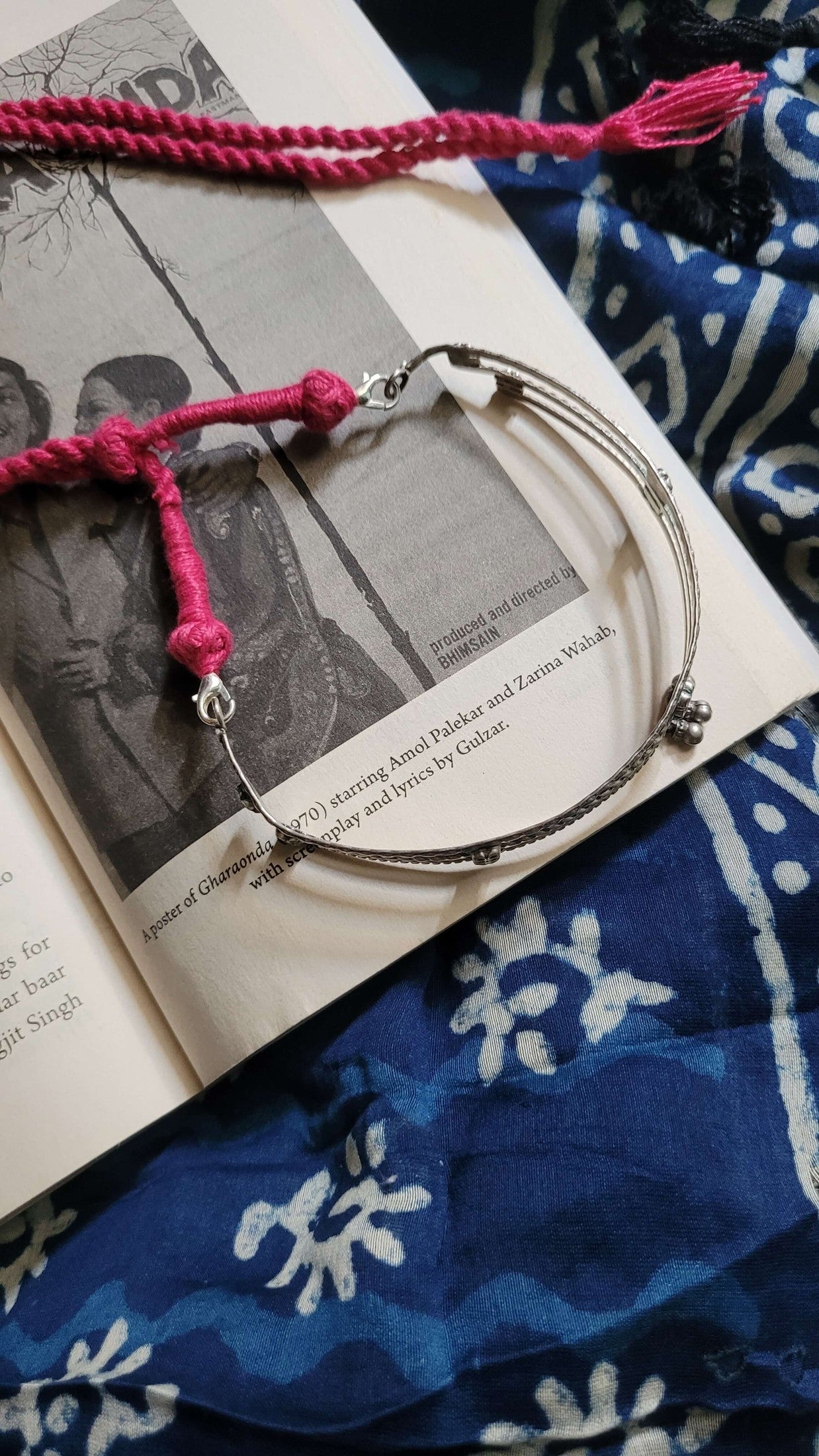 Kosha Choker with pink cord on an open book with a blue patterned fabric background