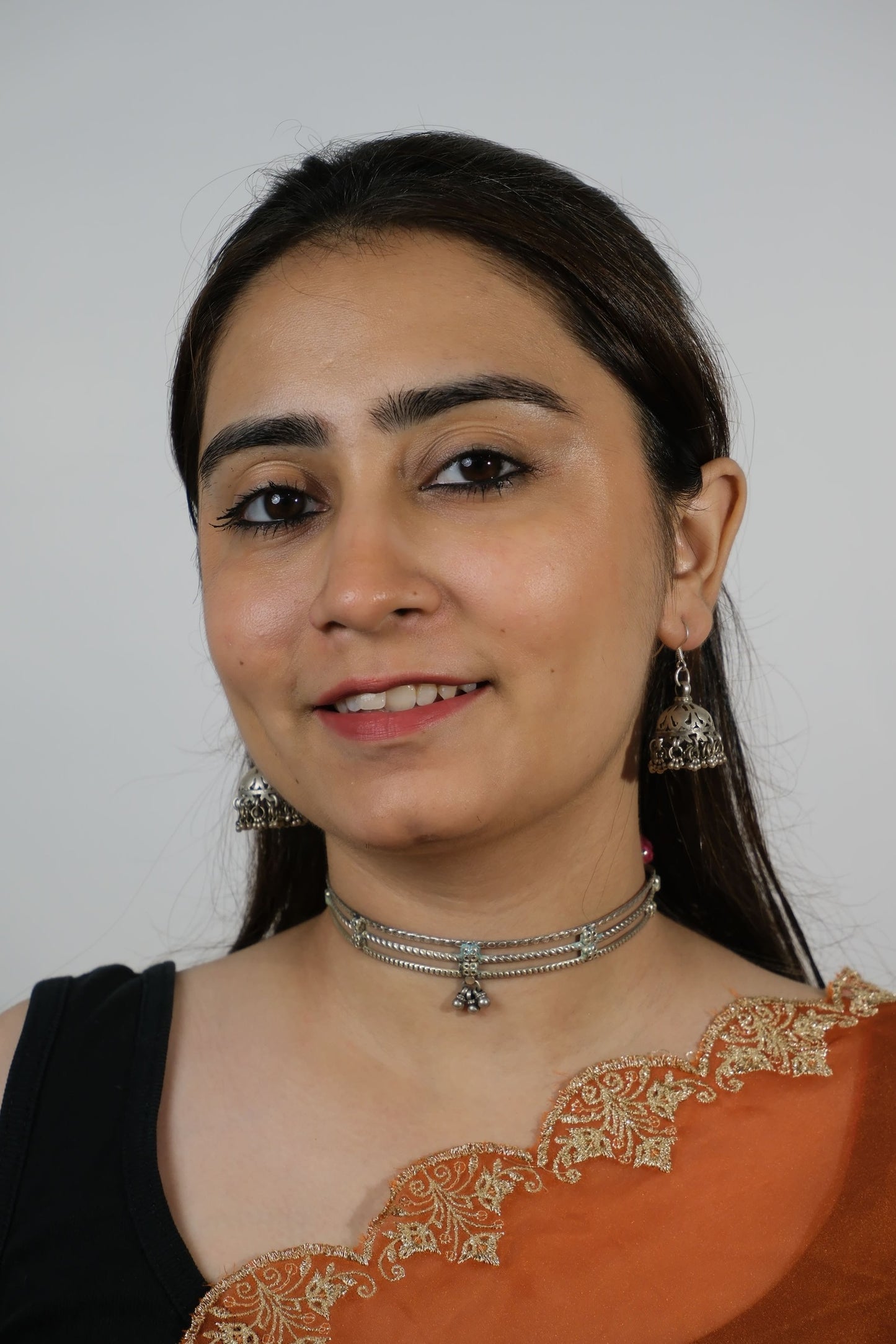 Woman wearing an orange saree with gold embroidery on a plain background