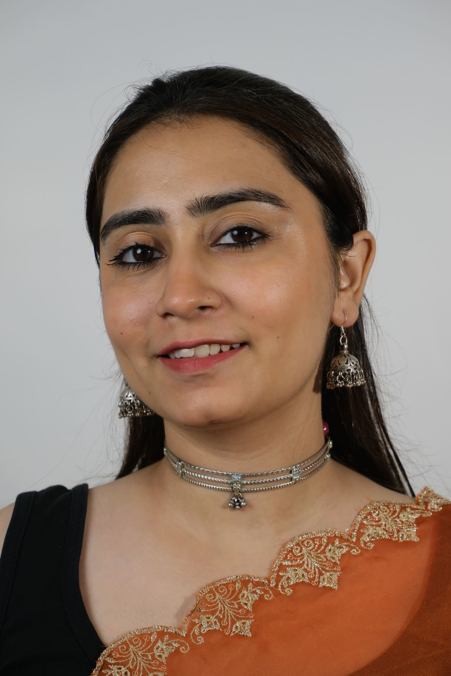 Woman wearing an orange saree with gold embroidery on a plain background