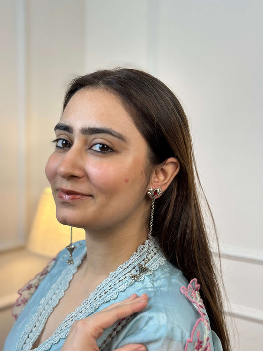Woman wearing earrings and a light blue top with lace details.