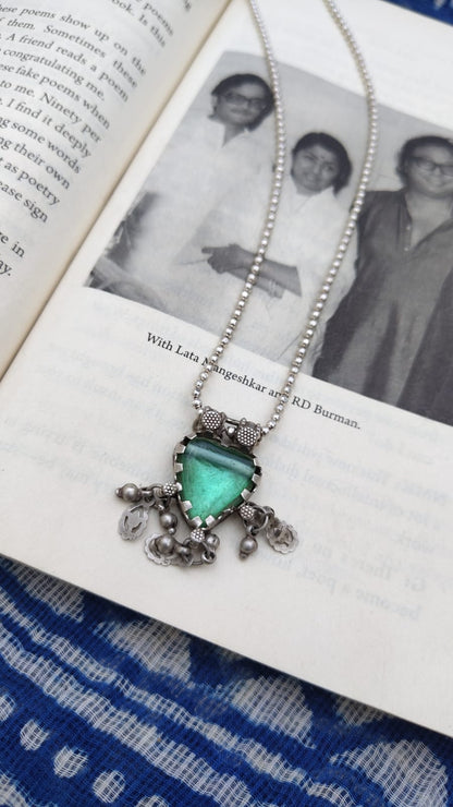 Necklace with a green pendant on an open book with a black and white photo inside.