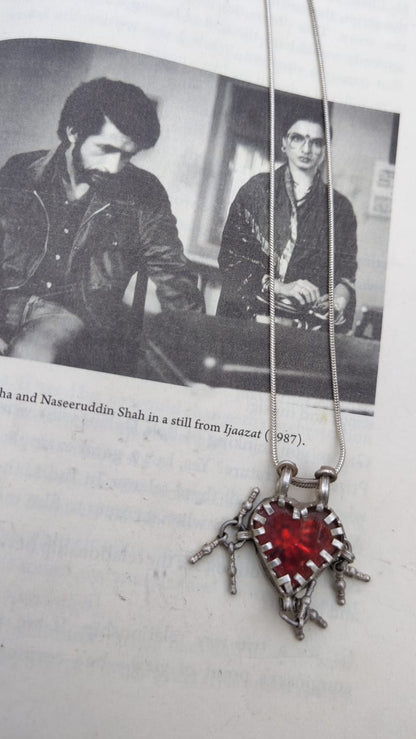 Necklace with a red heart pendant on a magazine page with black and white photos of two men.