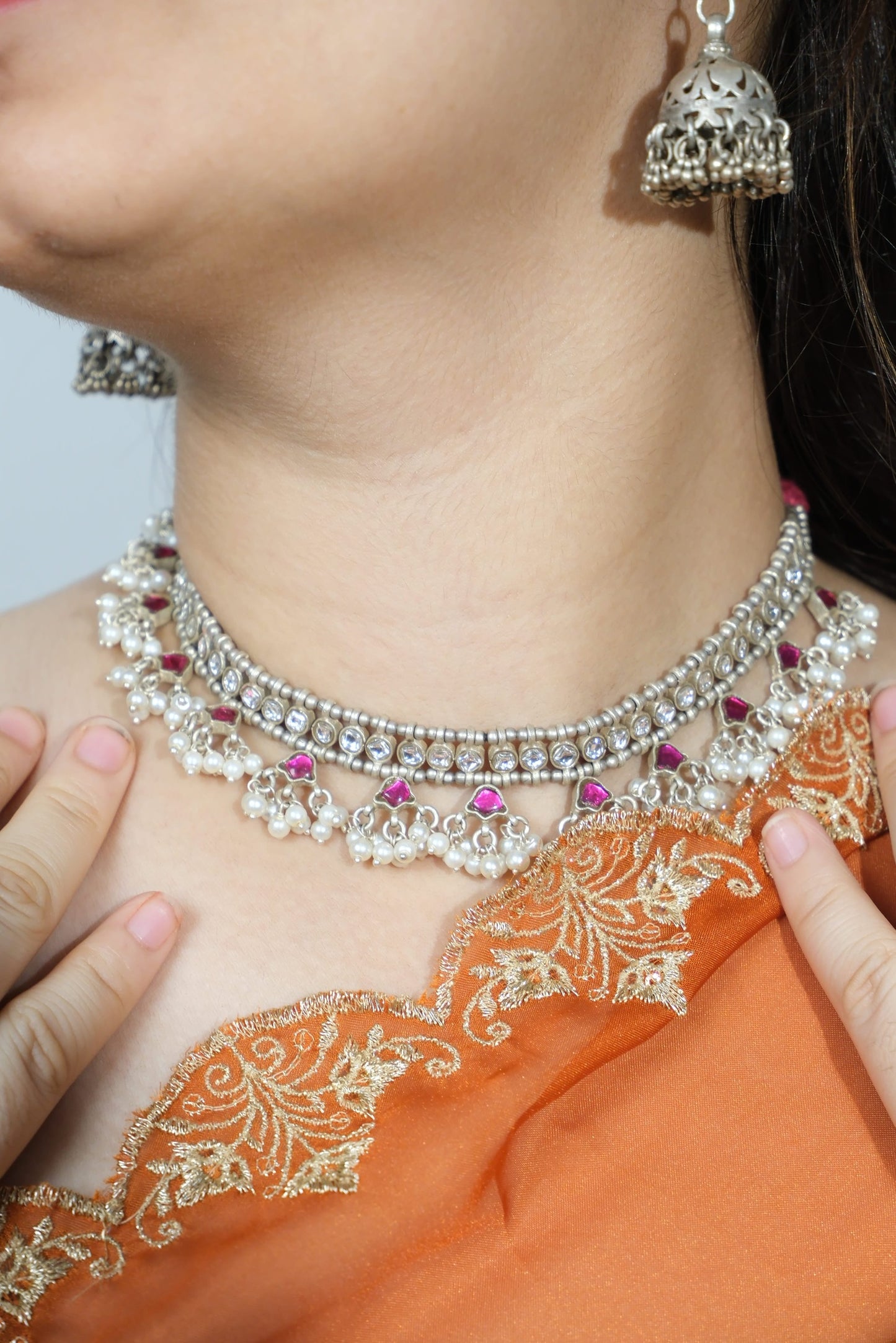 Close-up of a person wearing a silver necklace with pink stones and orange fabric.
