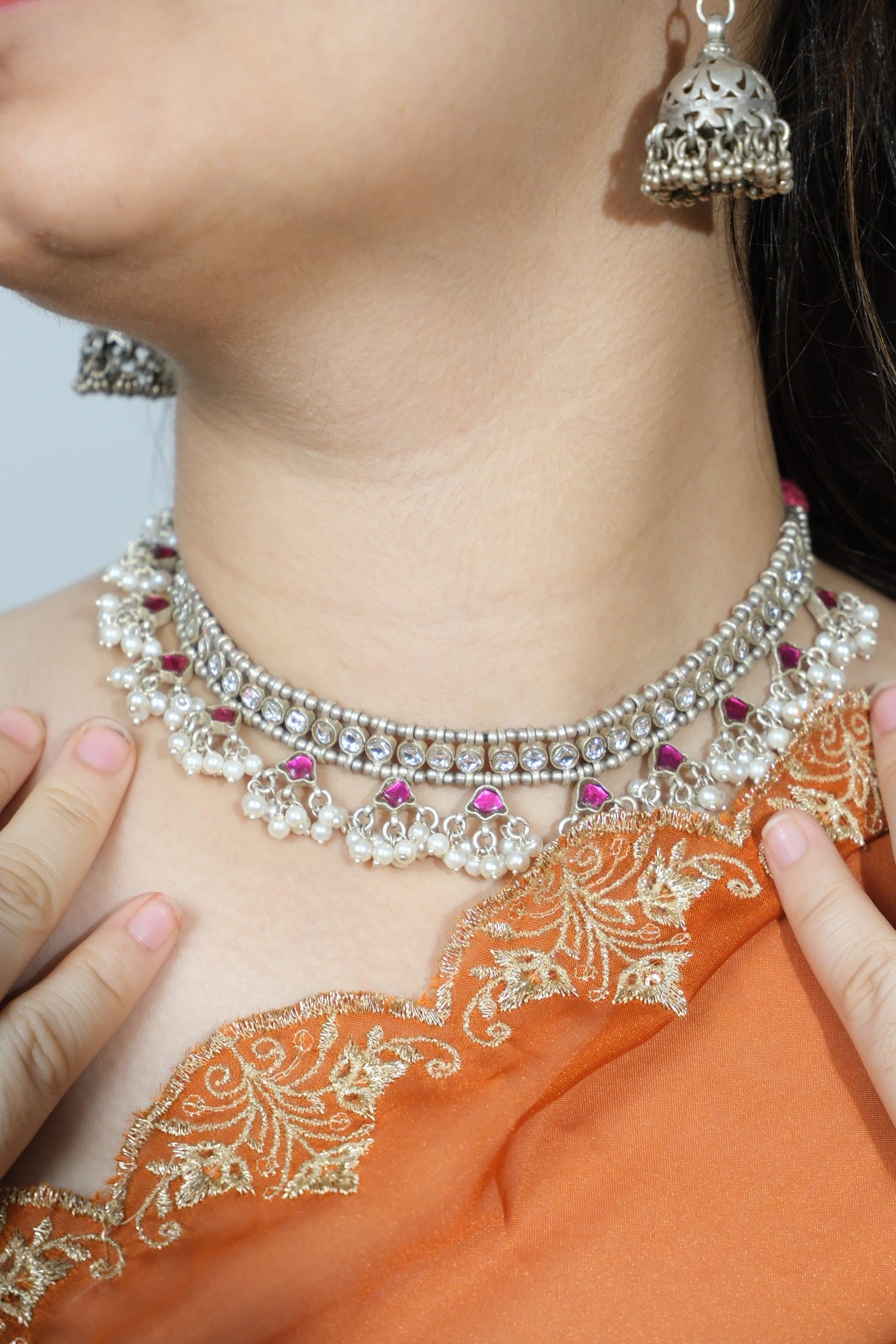 Close-up of a person wearing a silver necklace with pink stones and orange fabric.