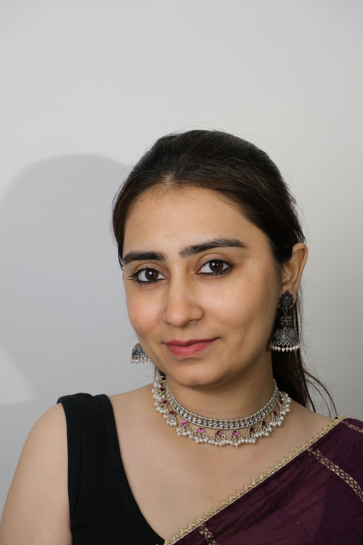 Woman wearing a black and purple traditional outfit with jewelry on a plain background