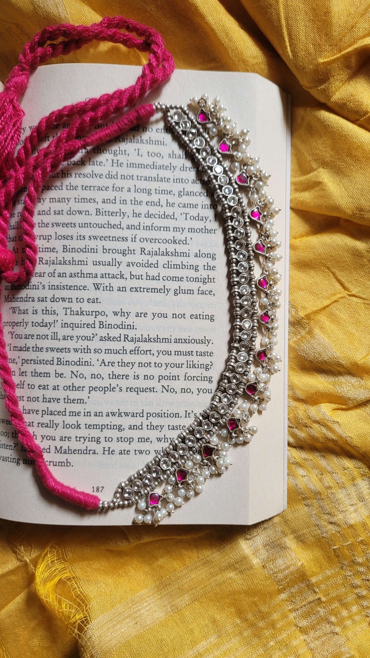 Madhubala Kundan Choker Necklace with pink and white stones on an open book against a yellow fabric background