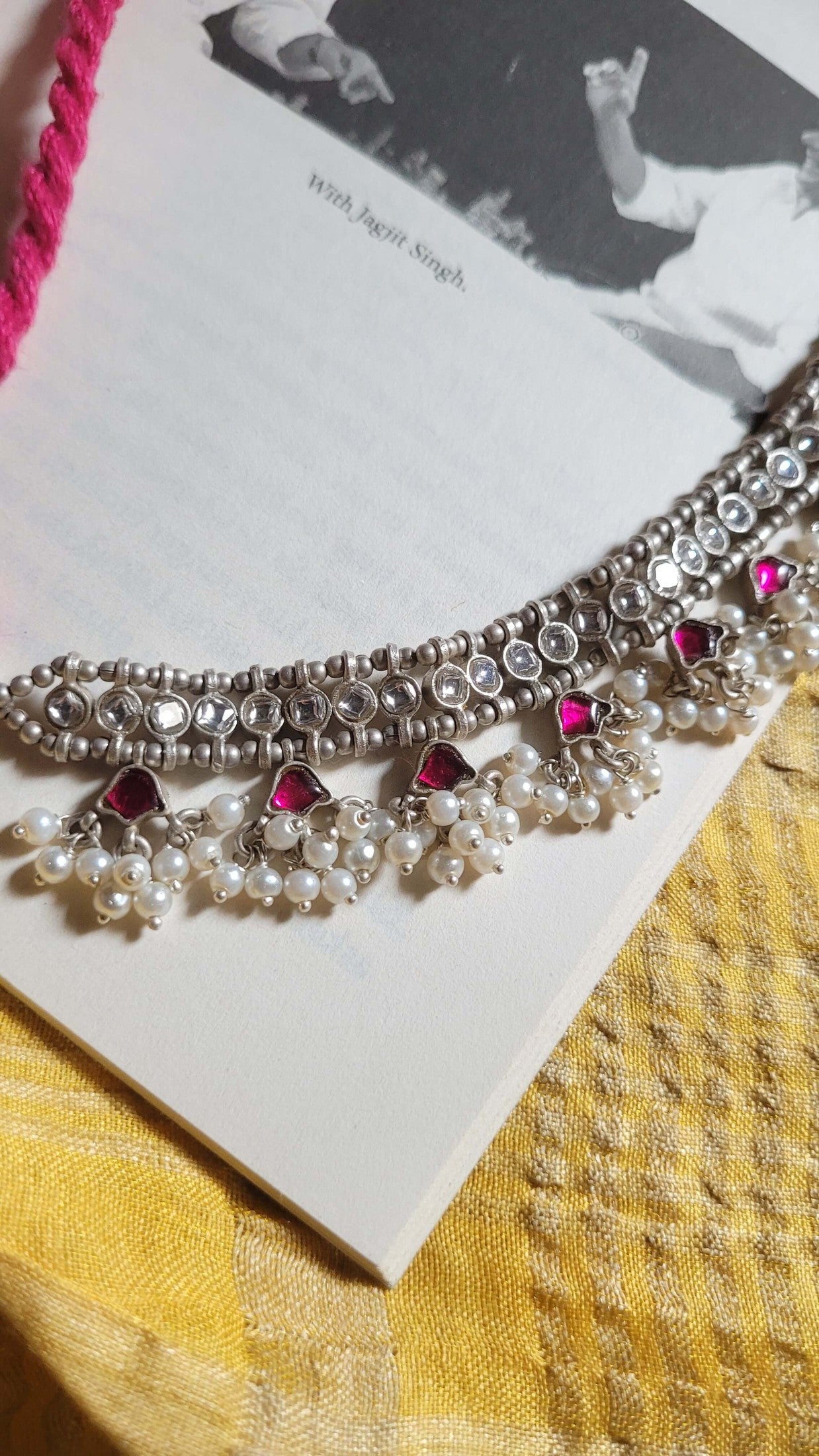 Decorative necklace with pearls and pink stones on a book and yellow fabric background