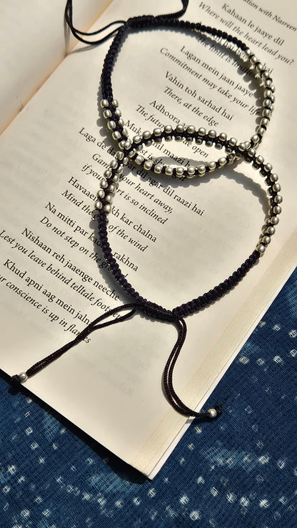 Black beaded anklets on an open book with a blue fabric background