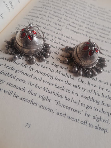 A pair of silver-toned beaded earrings with red gemstone accents, displayed on an open book page.