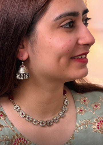 A woman in profile wearing a silver-toned traditional necklace and matching dangle earrings, with a light green embroidered blouse. 