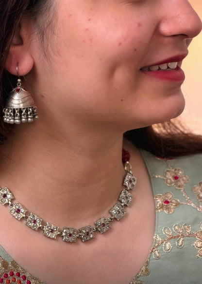 A woman in profile wearing a silver-toned traditional necklace and matching dangle earrings, with a light green embroidered blouse. 